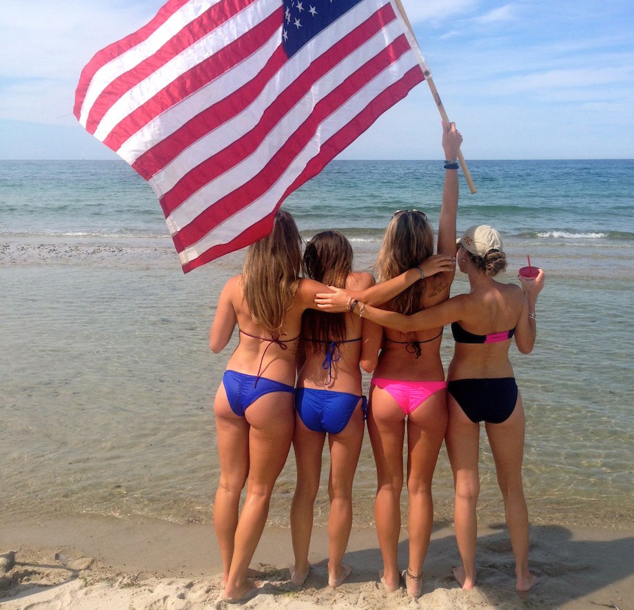 Chivettes in bikinis wave American flag at beach