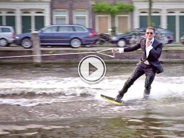 Picture of video of blonde guy in Amsterdam sporting shades and a black suit wake boarding.