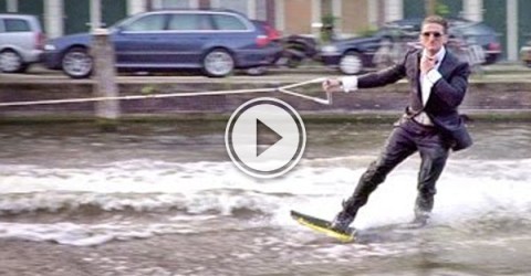 Picture of video of blonde guy in Amsterdam sporting shades and a black suit wake boarding.