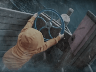 Kid in brown hoodie manning the steering wheel in a boat.