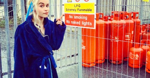 Emilia Clarke in blue bathrobe pointing to a danger sign