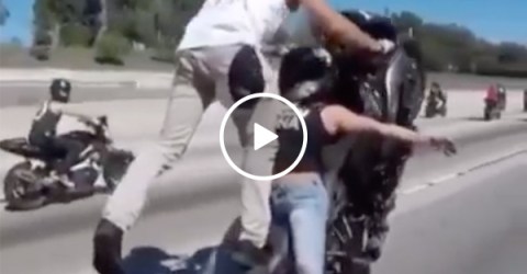 Woman balances on motorcycle as man pops a wheelie in tandem stunt